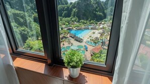 Ein Fenster mit Blick auf ein Feriengebiet, einschließlich eines Schwimmbads und üppiger Bepflanzung.