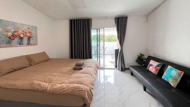 Ein Schlafzimmer mit Bett, einer Couch, einem Gemälde und Blick durch ein Fenster.