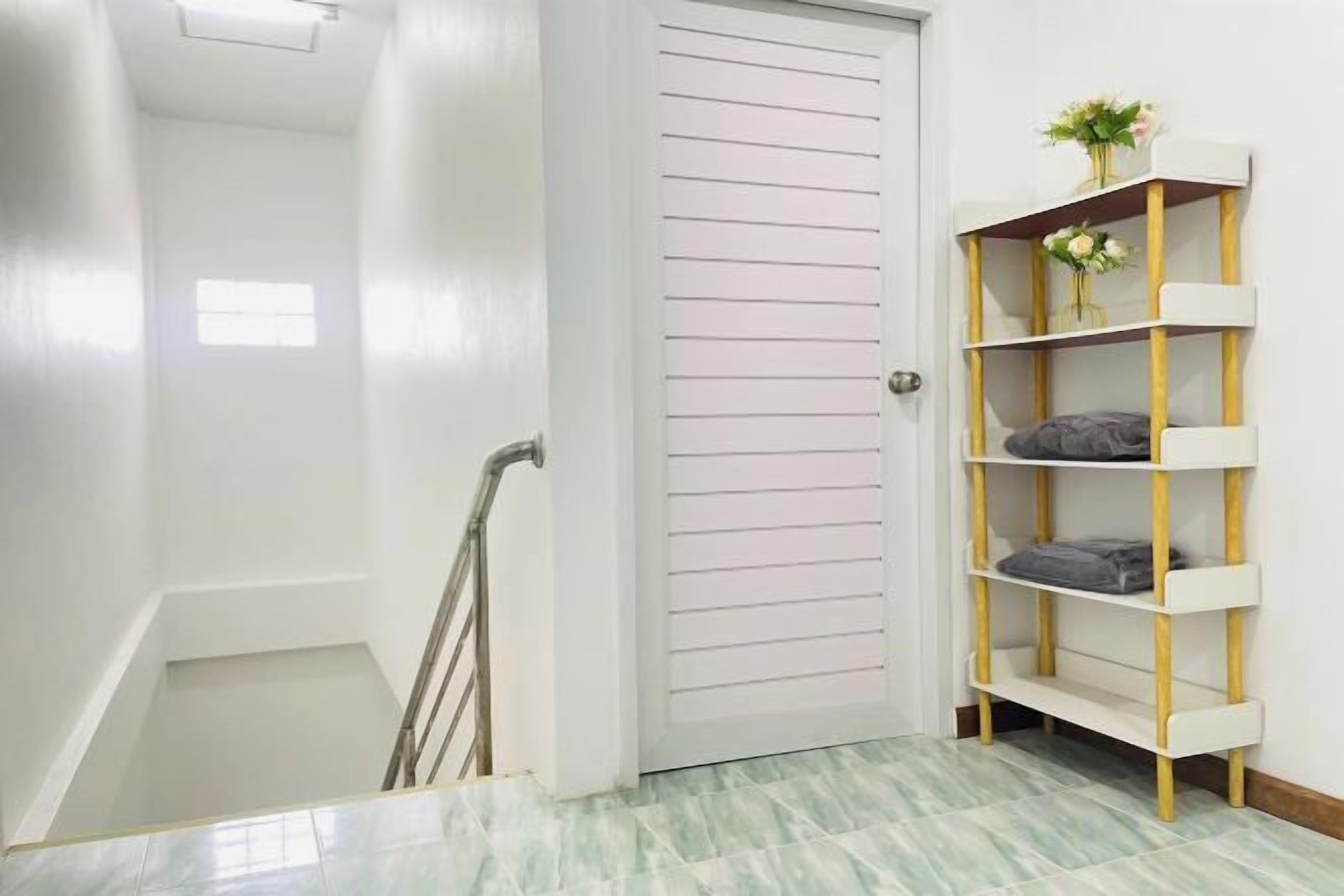 A hallway with a white door, a staircase, and a white and gold shelf unit with a vase of flowers.