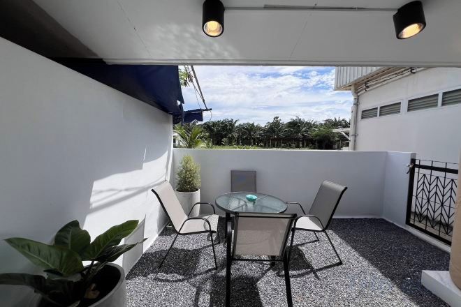 A balcony with a table and chairs, a potted plant, and a view of the sky and trees.