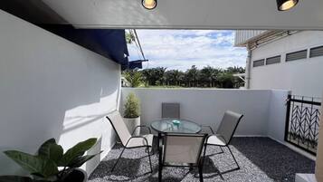 A balcony with a table and chairs, a potted plant, and a view of the sky and trees.