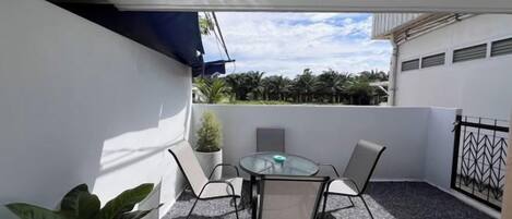A balcony with a table and chairs, a potted plant, and a view of the sky and trees.