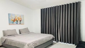 Ein Schlafzimmer mit einem Bett, einem Bild an der Wand und einem Fenster mit vertikalen Jalousien.