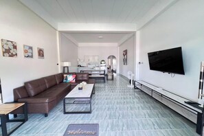 A modern living room with a sofa, coffee table, and a flat-screen TV mounted on the wall. - Kuan Mapraw Villa 2 (Phatthalung)