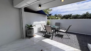 Eine moderne Terrassengruppe im Freien mit einem weißen Tisch und Stühlen, einem Blumentopf und Blick auf Palmen und einen klaren Himmel.