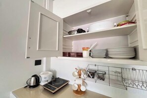 A kitchen with a microwave, kettle, and a kettle on the counter. There is a shelf with plates and a rack with utensils. - Kuan Mapraw Villa 2 (Phatthalung)