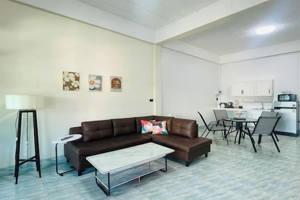 A living room with a brown sectional sofa, a coffee table, and a dining area with a table and chairs. - Kuan Mapraw Villa 2 (Phatthalung)