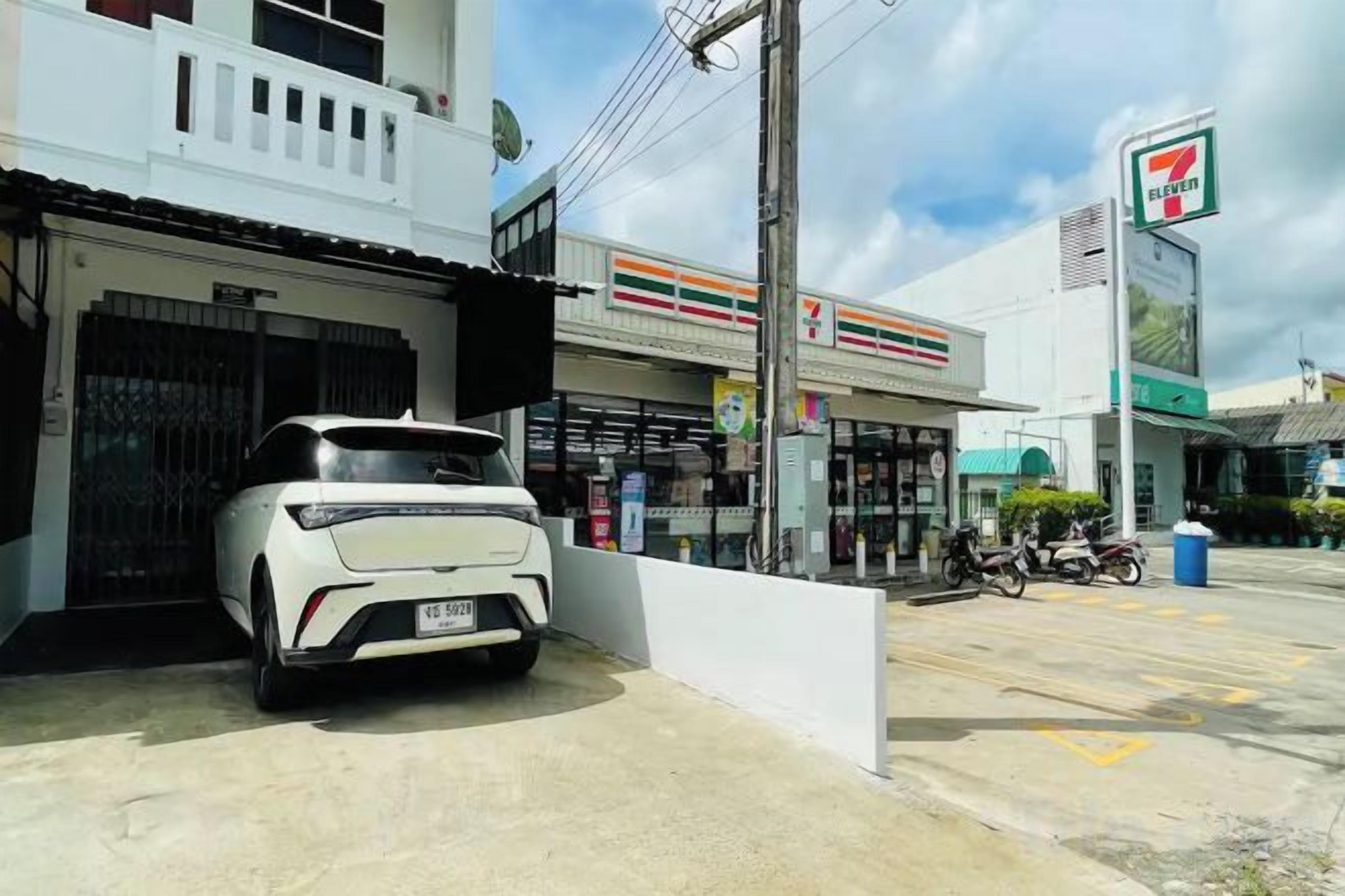 A white car parked in front of a building with a 7-Eleven store in the background.