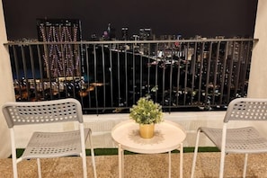 Un balcon avec deux chaises et une petite table, d’où l’on peut admirer la vue sur la ville illuminée la nuit.