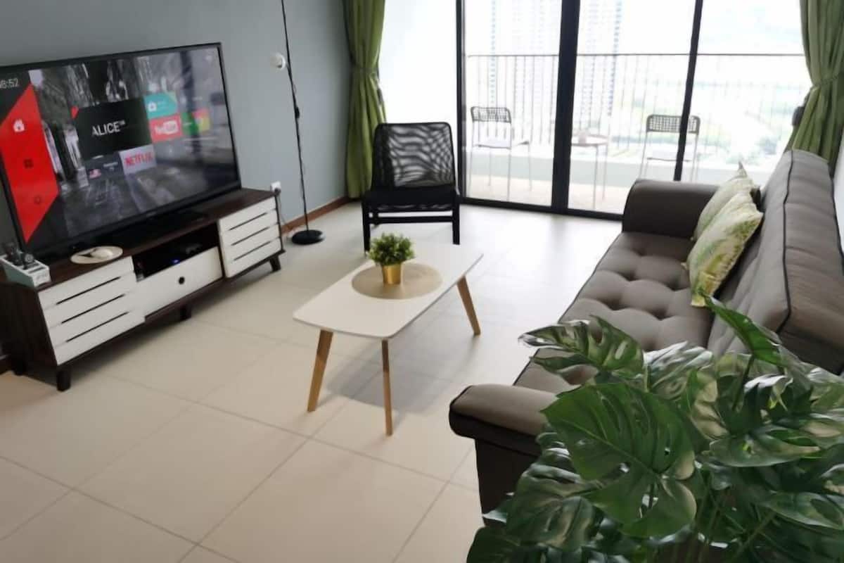 Un salon comprenant un téléviseur, un canapé, une table basse, un fauteuil et une grande plante.