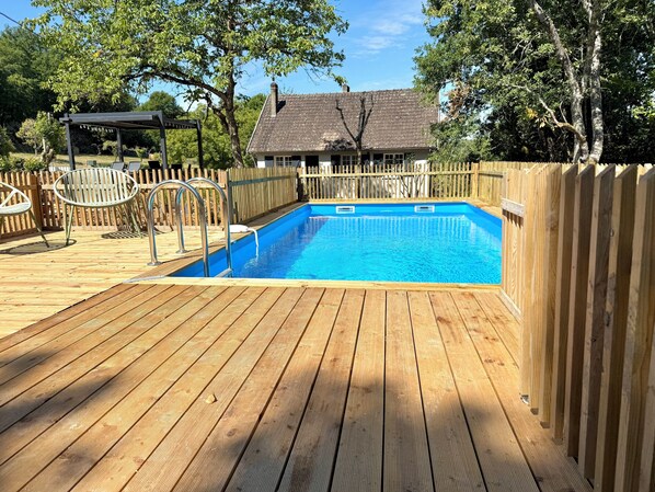 Une terrasse en bois avec une piscine, entourée d’une clôture en bois et d’arbres.