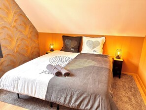 Un lit bien fait, avec une literie à motifs, deux lampes de chevet et des coussins décoratifs.