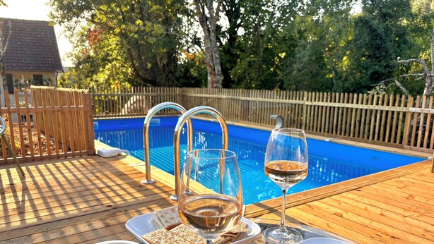 A wooden deck with a swimming pool, a glass of wine, and a table with food and a bowl of blueberries. - Villa Hakuna Matata heated pool 4 bedrooms near Périgueux in a quiet location (Château-l'Évêque)