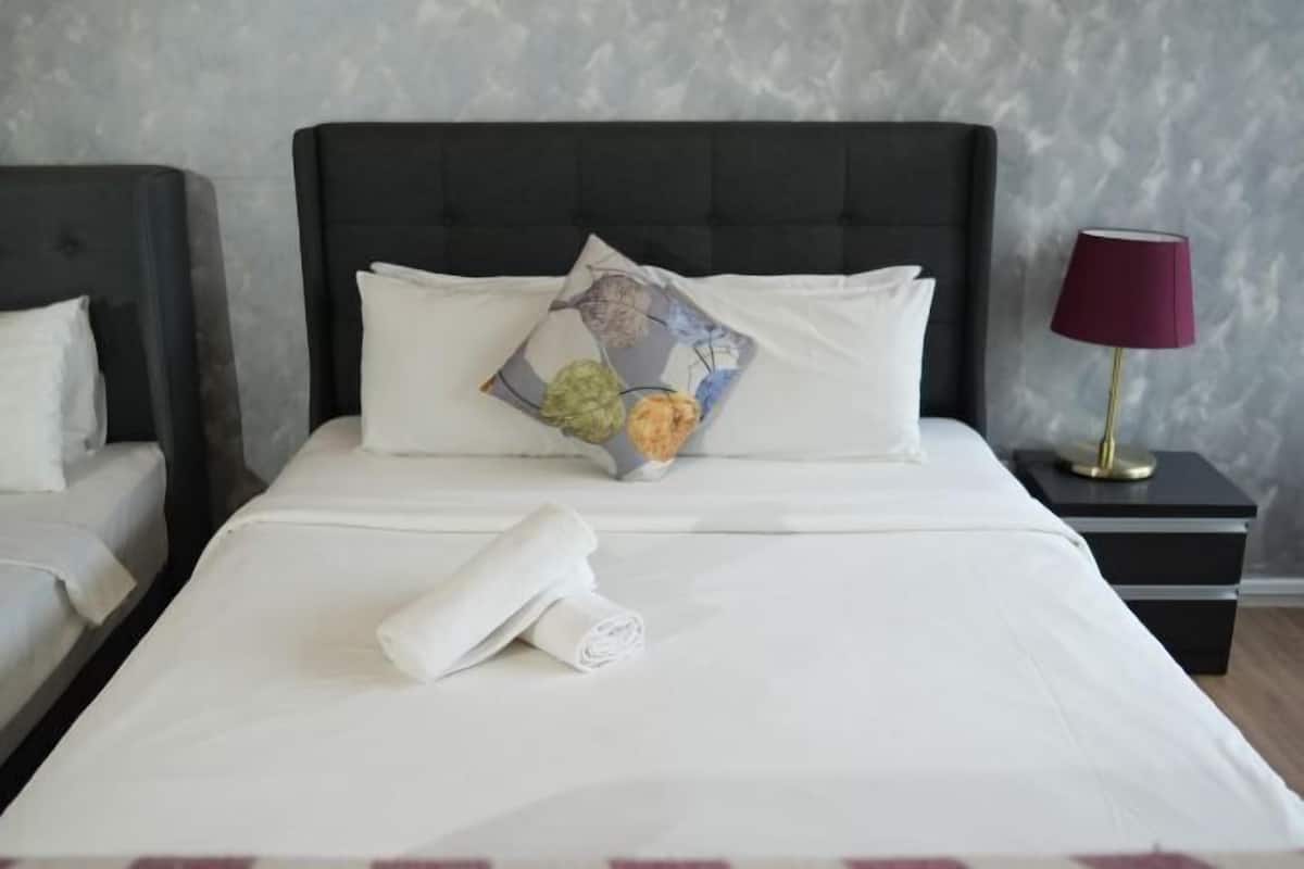A neatly made bed with white linens, a decorative pillow, and a rolled towel. There is a bedside table with a lamp and a nightstand with a lamp. The room has a textured wall and a dark headboard.