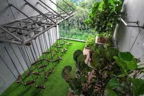 A room with a green artificial turf floor, a metal structure with hanging elements, and a view of greenery outside. - Ceylonz Suites Bukit Bintang By ICEFLY (Kuala Lumpur)