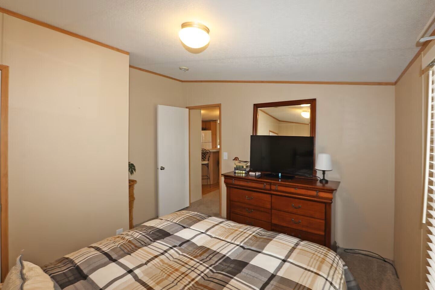 Ein Schlafzimmer mit Bett, Kommode, Fernseher und einer Tür zu einem Badezimmer.
