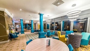 Ένα ξενοδοχειακό λόμπι με ένα στρογγυλό τραπέζι, μπλε και κίτρινες καρέκλες και μεγάλα παράθυρα.