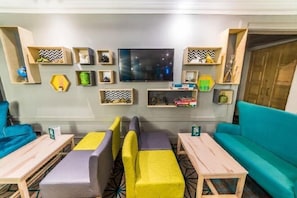 Une pièce comprenant un canapé, deux fauteuils, une petite table et un téléviseur fixé au mur.