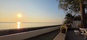 Une vue sur la mer avec un coucher de soleil, un mur blanc et un espace détente avec des tables et des chaises.