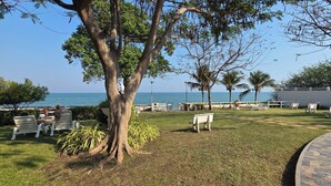 A grassy area with white chairs and a bench, a tree, and a view of the sea. - VIP Condominium GoldenEye - Hua Hin/Cha-am - TOP VIEW on beach/city/mountains (Tambon Cha-am)