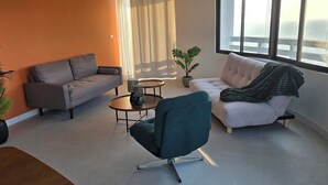 A modern living room with a grey sofa, a teal armchair, a small round table, and two potted plants. - VIP Condominium GoldenEye - Hua Hin/Cha-am - TOP VIEW on beach/city/mountains (Tambon Cha-am)
