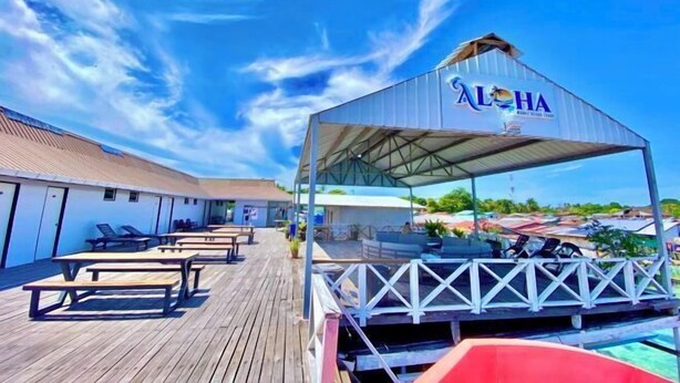 A covered outdoor area with a pool, lounge chairs, and a building with a sign reading "ALOHA". - Aloha MABUL Scuba Lodge (Semporna)