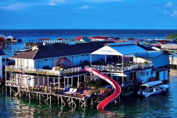 A floating hotel with a red slide, multiple levels, and a view of the ocean.
