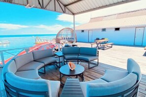 Un espace extérieur abrité, aménagé avec des tables et des chaises, et offrant une vue sur l’océan, notamment une table ronde et plusieurs chaises.