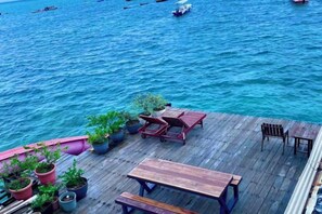 Terraza de madera con plantas en macetas y mobiliario exterior con vista a un cuerpo de agua.
