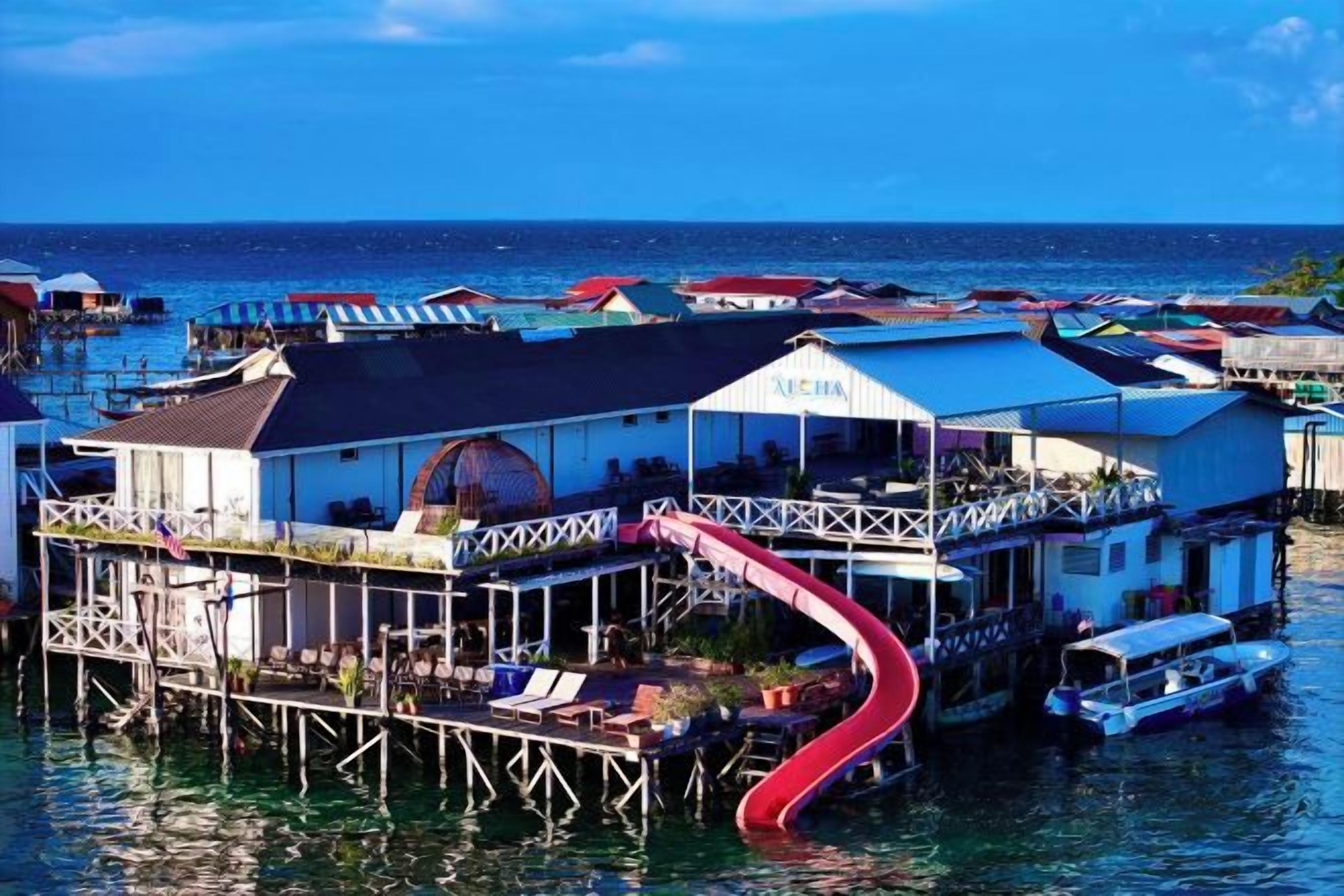 A floating house with a red slide leading to a deck, surrounded by water and other similar structures.