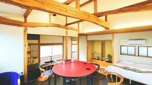 Una habitación con vigas de madera a la vista, una mesa redonda roja con cuatro sillas, una cama con colchón blanco y un ventanal con vistas.