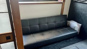 Un sofá de cuero negro en una esquina, con estructura de madera y suelo de baldosas.