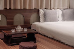 A neatly arranged bedroom with a bed, a small wooden table with a teapot and cups, and a cushioned bench. - CHI’S HOUSE (P. Hop giang)