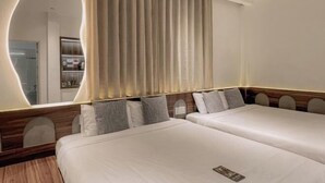 Une chambre d’hôtel avec deux lits, une tête de lit en bois, un grand miroir et vue sur la salle de bain.