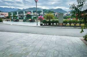 Un espacio peatonal empedrado con una carretera, un puente y montañas al fondo.