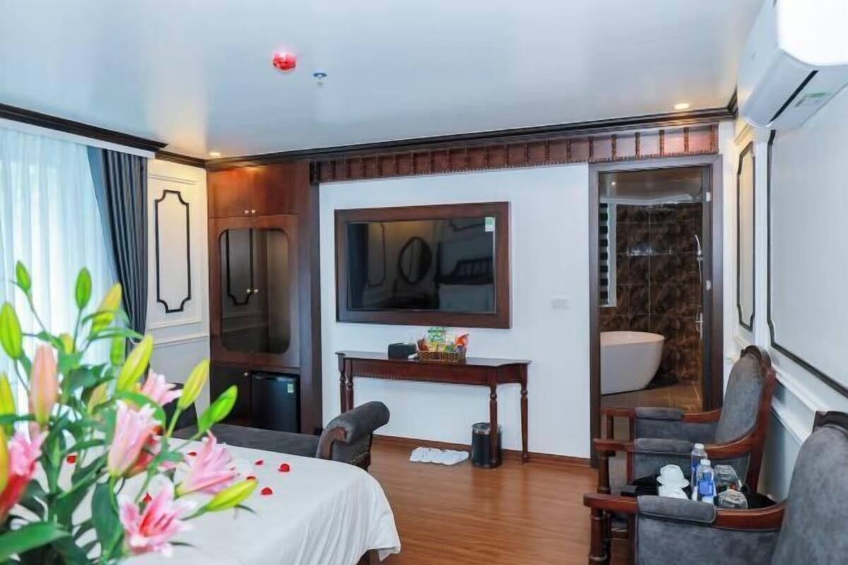 A hotel room with a bed, a desk, a chair, a large mirror, a window, and a bathroom.