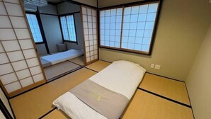 Ein traditioneller japanischer Raum mit Tatami-Boden, Futon-Bett, verschiebbaren Shoji-Türen und Blick durch ein Fenster mit Shoji-Gitter.