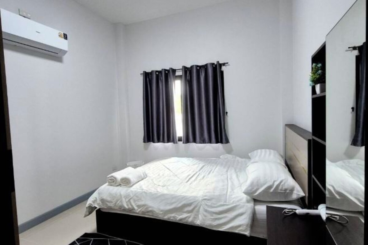 Una cama individual con ropa blanca, una mesita de noche, un espejo y una ventana con cortinas oscuras.