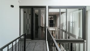 A modern interior with a glass door entrance, a staircase with a metal railing, and a view of a room with a bed and a nightstand. - INARA VILLA , Luxury Pool Villa Pattaya by Viola & Olivia (Pattaya)