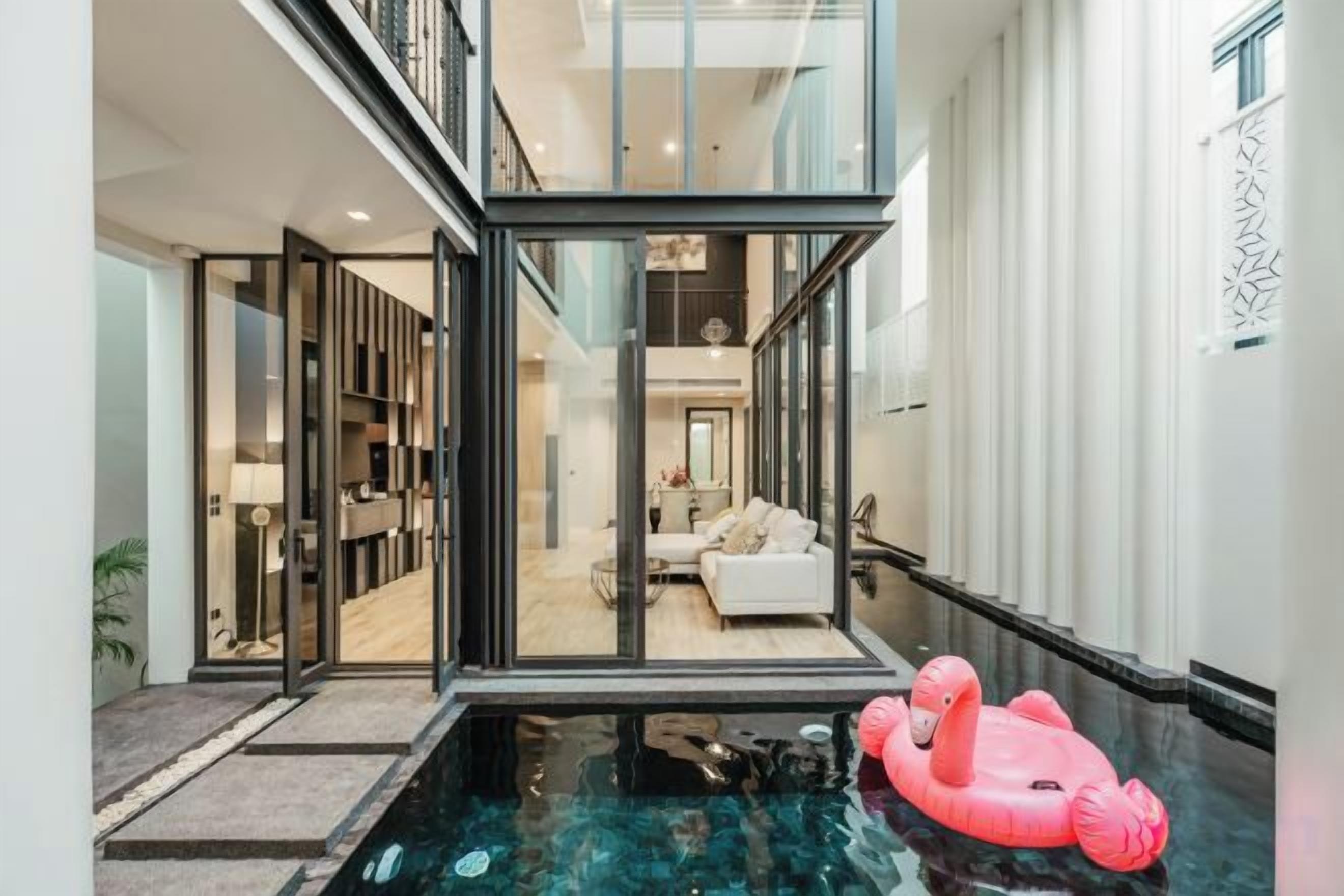 A modern interior with a glass-enclosed living area, a pool with a pink float, and a visible kitchen area.