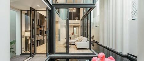 A modern interior with a glass-enclosed living area, a pool with a pink float, and a visible kitchen area.