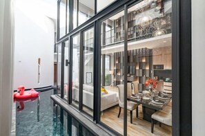 A modern interior with a glass-enclosed pool, a dining area with a table and chairs, and a kitchen visible through the glass. - INARA VILLA , Luxury Pool Villa Pattaya by Viola & Olivia (Pattaya)