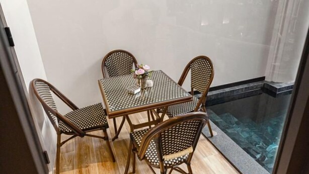 A small dining area with a table and four wicker chairs, a vase with flowers, and a glass partition with a view of a pool. - INARA VILLA , Luxury Pool Villa Pattaya by Viola & Olivia (Pattaya)
