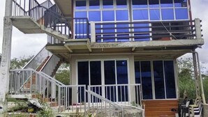 Ein zweistöckiges Gebäude mit Balkon, Treppe und einer Veranda mit Stühlen.