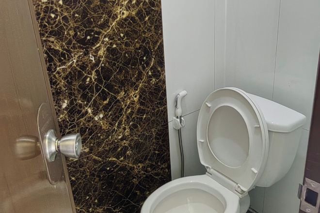 A bathroom with a marble wall, a white toilet, and a door with a silver handle.