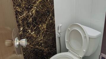 A bathroom with a marble wall, a white toilet, and a door with a silver handle.