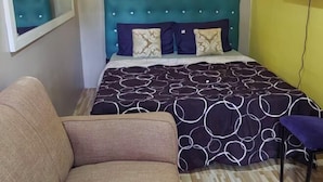 Ein Schlafzimmer mit einem türkis-bezogenen Kopfende, einer gemusterten Bettdecke und einem einzelnen Sofa mit Kissen.