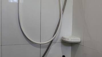 A shower area with a white tiled wall, a handheld showerhead, and a soap dish.