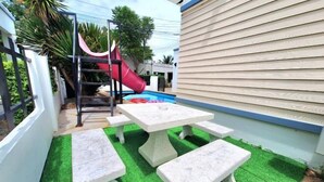 Un patio con piscina, tobogán y mesa con bancos.