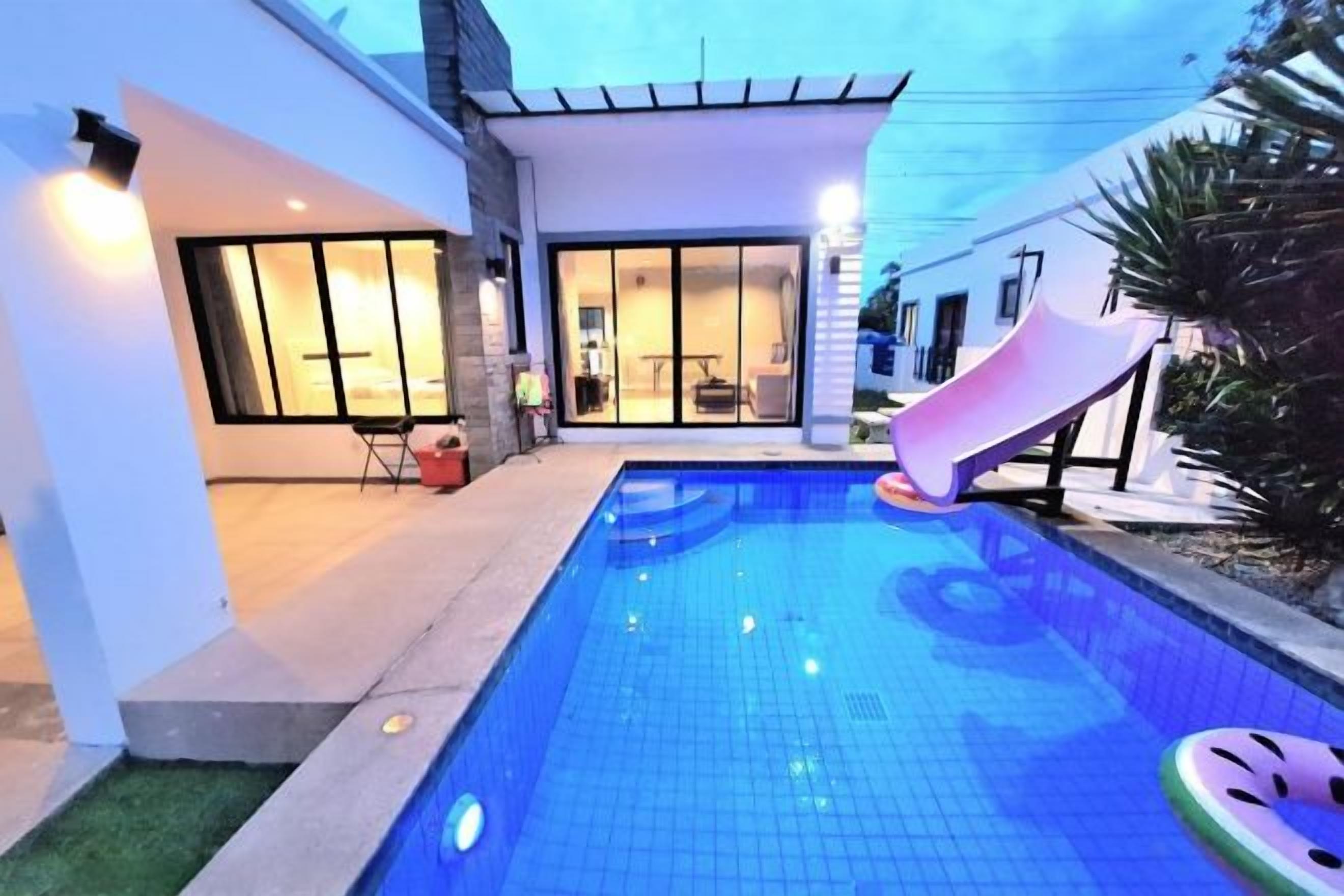 Una piscina con tobogán, un área de patio y un edificio con ventanales grandes.